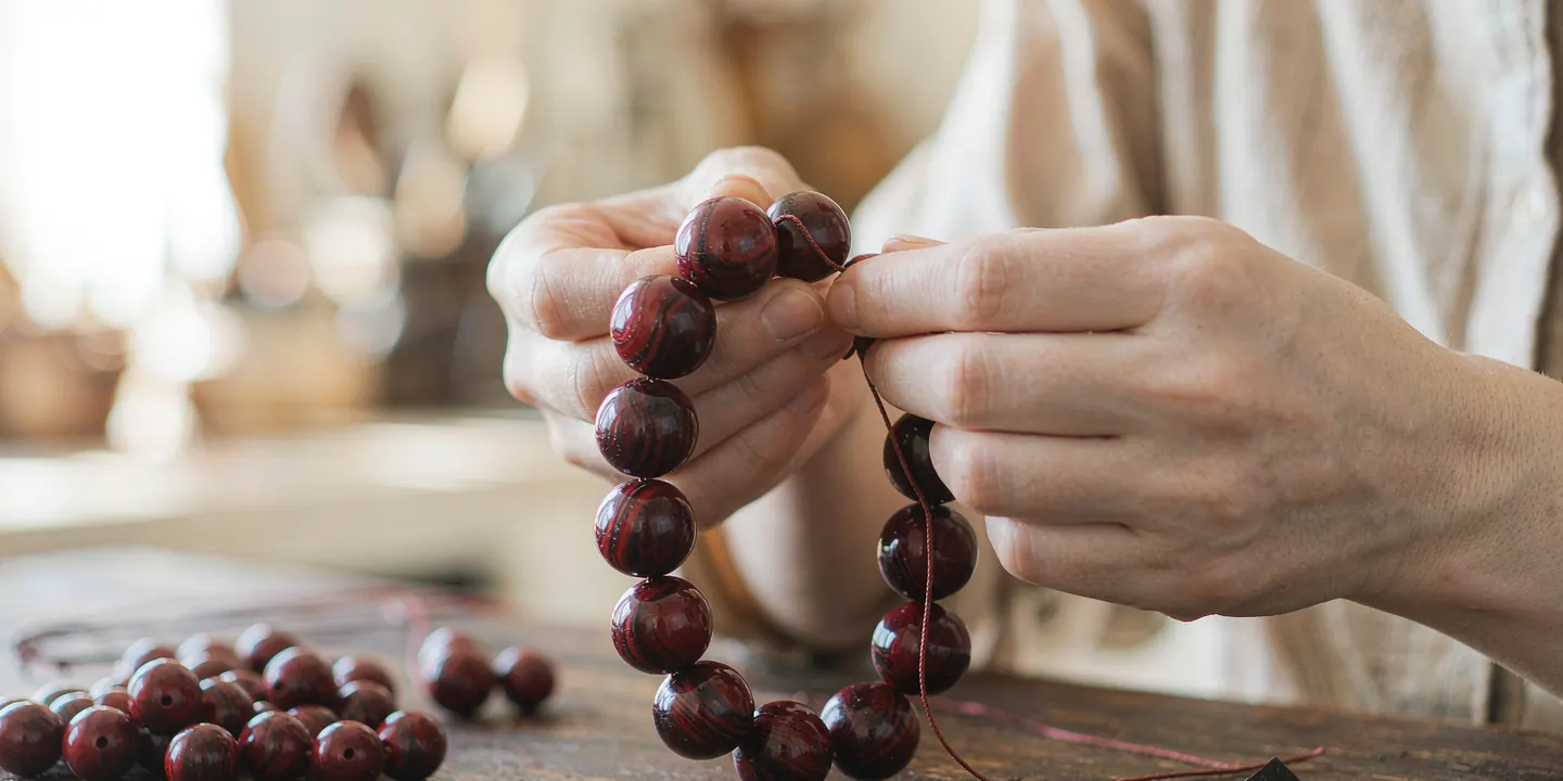 Des mains enfilant un bracelet de perles de cinabre sur un établi en bois